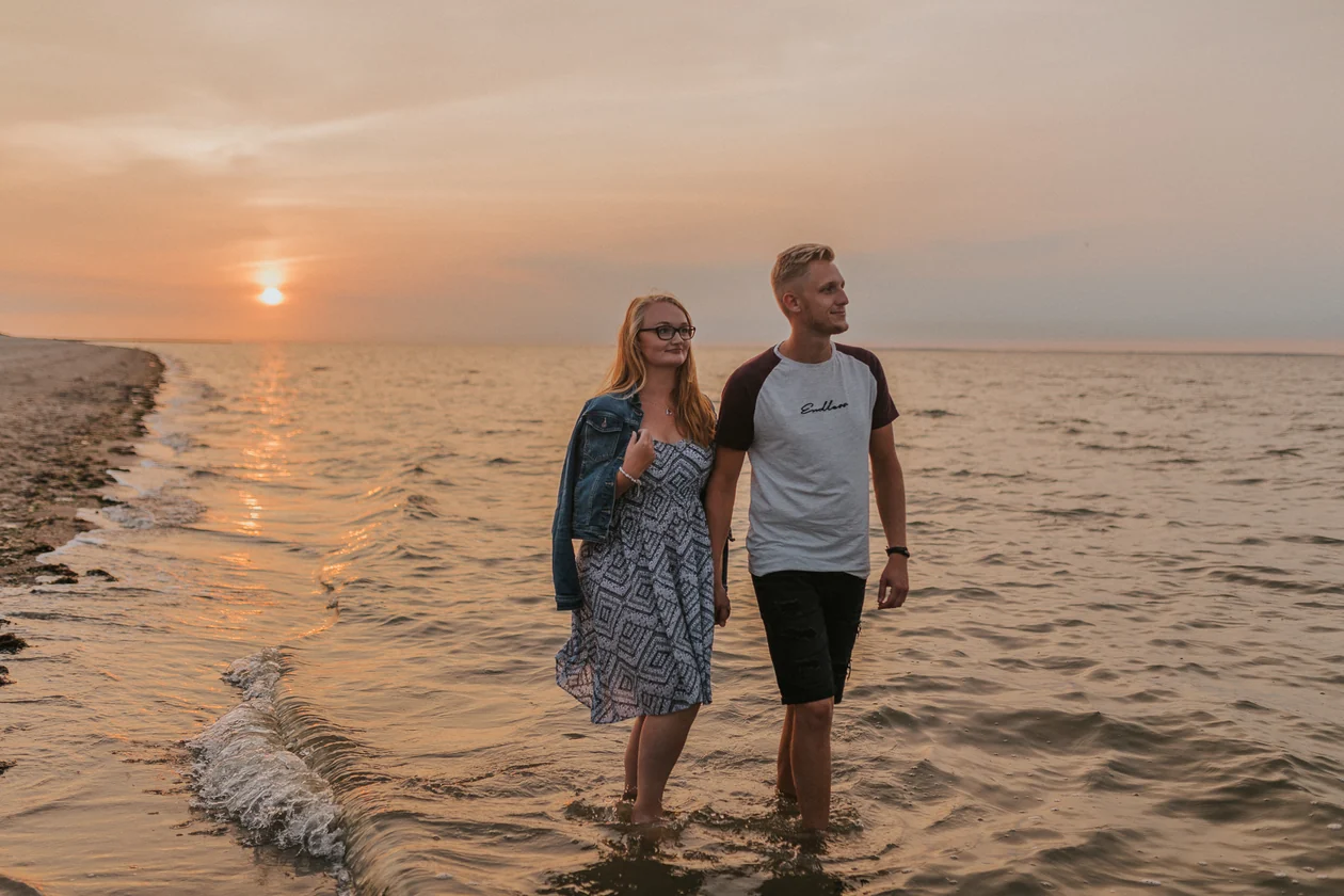 Paar hält sich am Wasser bei Sonnenuntergang an den Händen